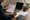 Person reviews a document and writes in a notebook beside an open laptop on a wooden desk.