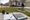 Person arranges decorative yard signs on a suburban lawn beside a patio table with a notebook and tape measure.