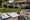 A person installs stakes in a suburban lawn beside planning materials, gloves, and colorful yard signs.