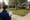 Person in a navy jacket and cap writes on a clipboard beside a suburban driveway and lawn.