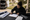 Woman fills out paperwork at a table beside an open van, with sign materials arranged nearby.