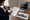 Person reviews paperwork beside a laptop and home listing photos at a wooden table.