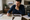 A man studies a map and property photo at a desk indoors.