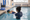 An adult supports a child wearing goggles near the edge of an indoor pool.