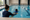 An adult swimmer reaches toward a child practicing in an indoor swimming pool.
