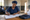 Woman in a navy head covering records information in a ledger at a wooden table inside a simple clinic.