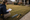 Person kneels on a suburban lawn, measuring the ground beside stakes, a mallet, and a clipboard.