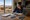 Woman reviews documents and property photos at a table beside a laptop, with a desert neighborhood outside.