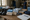 A person sorts packaged supplies in the background beside boots, folded towels, containers, and an open notebook.