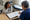 Two people review medical paperwork at a clinic table beside an examination bed.