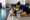 An adult kneels beside a seated young swimmer at the edge of an indoor pool.