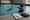 Swim instructor points toward a swimmer practicing in an indoor pool beside a clipboard and folded towel.