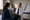 A clinician speaks with a seated patient while taking notes in a bright examination room.