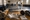 Fencers practice on a strip while masks, gloves, jackets, and foils rest on a nearby table.