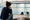 A seated woman watches a swimmer holding the pool edge in an indoor pool.
