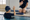 A swimmer and instructor raise their hands across the edge of an indoor pool.