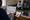 Person studies a printed timeline chart at a desk while two people confer in the background.