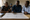 Three adults examine a hand-drawn diagram on a table, with one person pointing to its connected icons.