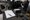 Person works inside a vehicle while a clipboard, stereo unit, speaker, and tools rest on a workbench.