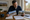 Man compares photographs of two houses while writing notes at a table with documents and a calculator.