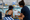 Adult and child sit beside an indoor pool, reviewing a clipboard together.