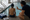 An instructor gestures beside a seated child at the edge of an indoor swimming pool.