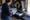 Woman checks a clipboard beside a bin of circular signs and supplies in a workshop.