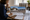 Woman reviews property photographs and documents at a desk beside a sunlit window.