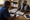 Two people sit at a wooden table, organizing bottles and packaged supplies while one writes notes.