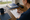 Person writes on a checklist beside graduation caps, tassels, notebooks, and coffee at a desk.