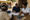 Three people review paperwork together at a wooden table outside a building, with notebooks and a case nearby.