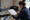 Woman reviews a clipboard at a desk beside sign designs and drafting materials.