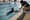 Swimmer practices reaching for the pool edge as an instructor kneels beside the indoor pool.