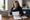 Woman reviewing printed documents beside an open laptop and coffee mug at a kitchen table.
