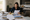 A woman reviews building plans and writes at a table beside a laptop in a kitchen.