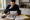 A man studies a document and property photographs at a kitchen table beside plans and a calculator.