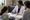 A clinician reviews paperwork with two women seated at a desk in an office.