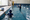 A child holds the pool edge while an instructor gestures across the indoor swimming pool.