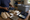 Hands hold a dark shoe above a table displaying slippers, folded textiles, supplies, and an open toiletry case.