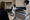 Two fencers face each other on a gymnasium piste while an observer watches nearby.