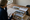 Person reviews home photographs and a map at a wooden table beside a window.