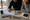 Two people review architectural plans and property photographs at a table beside a desert landscape.