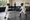 Two young fencers in masks practice with swords on an indoor fencing strip as an observer watches.