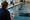 An adult observes a swimmer practicing in an indoor pool while holding a clipboard.